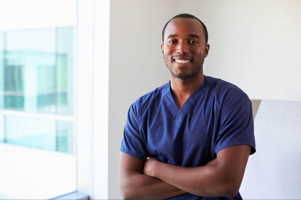 A black man in scrubs smiles at the camera.