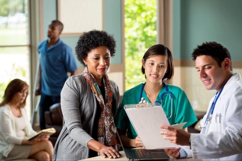 A small group of diverse healthcare professionals discuss the contents of a clipboard.