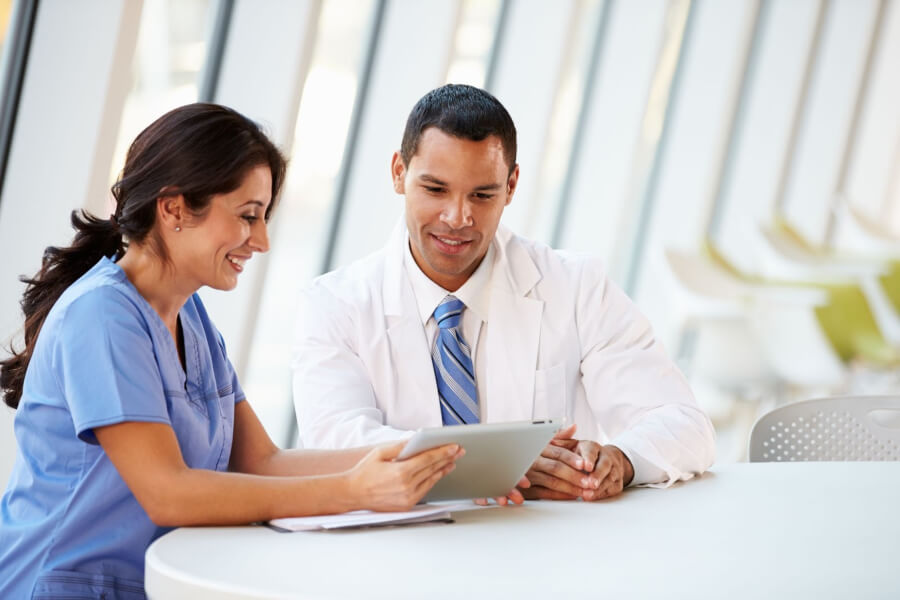 A woman in scrubs and a man in a lab coat sit at a table discussing healthcare opportunities.